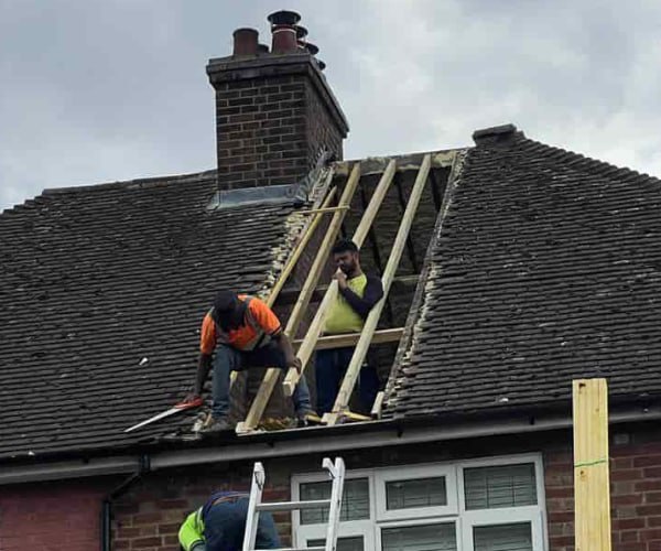 This is a photo of a roof repair being carried out. A section of the roof has been stripped and two roofers are replacing the rafters. Works being carried out by KJI Roofing Rothwell